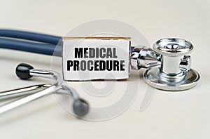 On a gray background, a stethoscope and a cardboard sign with the inscription - Medical Procedure