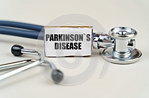 On a gray background, a stethoscope and a cardboard sign with the inscription - Parkinsons disease