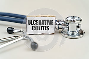 On a gray background, a stethoscope and a cardboard sign with the inscription - Ulcerative colitis