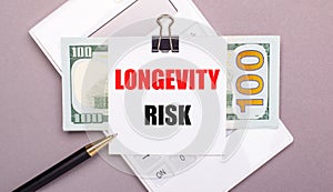 On a gray background, a white calculator, a pen, banknotes and a sheet of paper with the text LONGEVITY RISK.