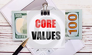 On a gray background, a white calculator, a pen, banknotes and a sheet of paper under a black paper clip with the text CORE VALUES