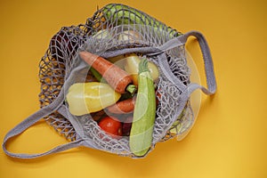 Gray bag string bag with vegetables,zucchini,bell peppers,carrots,beets,onions yellow background.Harvest from garden fresh bright