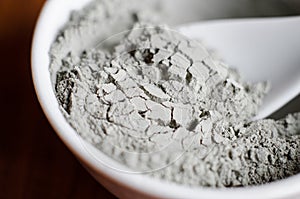Gray bentonite clay powder in a bowl. Diy facial mask and body wrap recipe. Natural beauty treatment and spa. Clay texture closeup photo