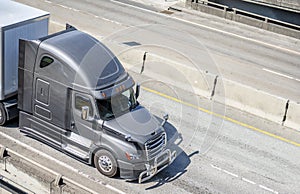 Gray big rig long haul semi truck transporting semi trailer with commercial cargo running on wide multiline highway