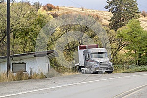 Gray big rig semi truck with dry van semi trailer standing on the driveway to the house on the side of the highway waiting for the
