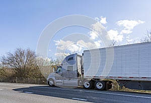 Gray big rig semi truck with refrigerated semi trailer standing of road on road shoulder