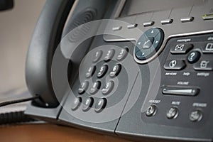 Gray and black business wired phone with receiver, dial and large display in the business office environment