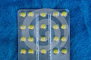 Gray blister with yellow pills on blue woolen background