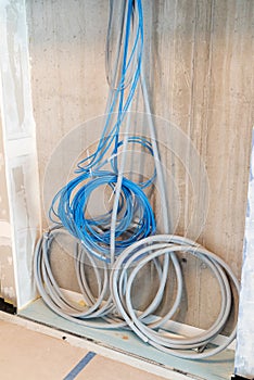Gray and blue electrical cables hanging on a wall in spirals and bundles