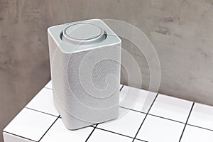 A gray bluetooth speaker, square, music column stands on a tile of white squares photo