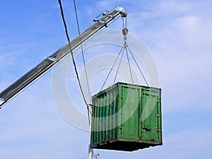 Gray boom with blue hook of  truck manipulator lift green cargo container up