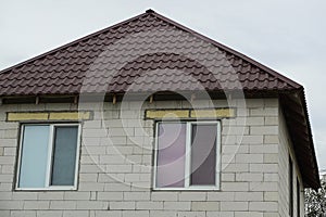 Gray brick attic of a private house with two windows under a brown tiled roof