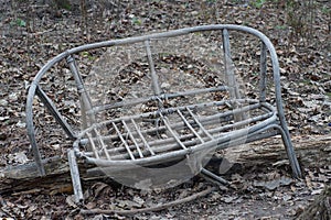 A gray broken wicker wooden chair stands on the ground and dry leaves