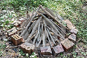 Gray and brown firewood for a bonfire are in a round fire with orange bricks on green grass in a summer forest. like a pyramid