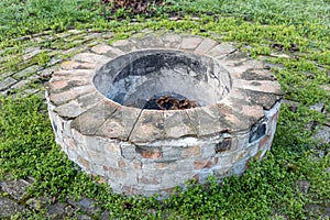 Gray and brown round fire hearth with orange bricks for a bonfire on green grass in a summer forest