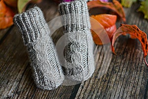 Gray cable knit baby socks on dark wooden background and dry autumn leaves