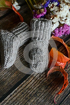 Gray cable knit baby socks on dark wooden background and dry autumn leaves