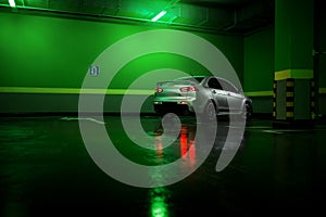 Gray car stay at underground parking lot and reflect in wet asphalt