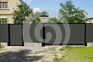 Gray closed metal gate and door with part of the fence