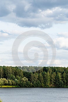 Gray clouds in blue sky over forest on lake coast