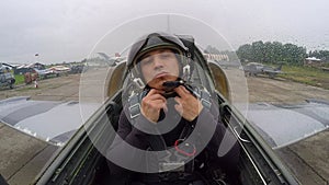 Gray combat fighter plane standing at the old airfield. Navigator man adjusts and fixes the helmet of the pilot. Inside view