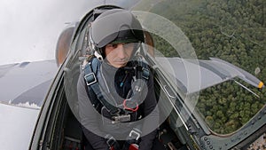 A gray combat jet plane fly over field and river and rolls to the left. Caucasian pretty man in a helmet â€“ navigator of pilot