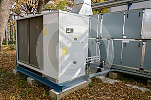 Gray commercial air handling unit with big condensing unit standing outdoor on the ground covered by fallen leaves