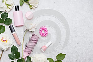 On a gray concrete background a set of cosmetics is laid out in a mix with flowers and green leaves, copy space