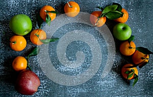 Gray concrete background, tangerines with leaves and twigs, red and green apples view from the top. Place for an