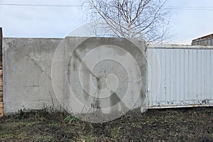 Gray concrete fence wall and part of a white metal gate