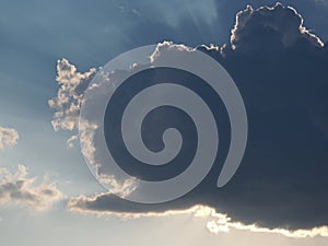 Gray cumulus on a blue sky covering the sun with sun rays coming out from behind the cloud