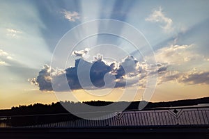 Gray cumulus on a blue sky covering the sun with sun rays coming out from behind the cloud. A large gray-white cloud with bright