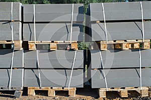 Gray curbs, concrete blocks on pallets for road repairs, outdoors. Construction Materials