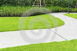 The gray curve pattern walkway in a beautiful garden, sand washed finishing on concrete paving, a smooth green grass lawn, trees