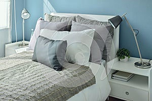 Gray, dark gray and beige pillows on bed with blue wall