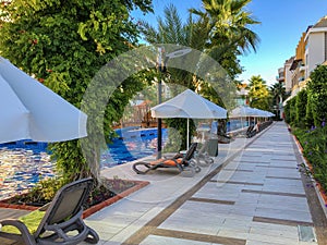 Gray deck chairs with an orange cushion by the pool with white umbrellas from the sun