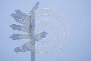 Gray direction sign pointing on capitals of countries on a gray foggy sky background.