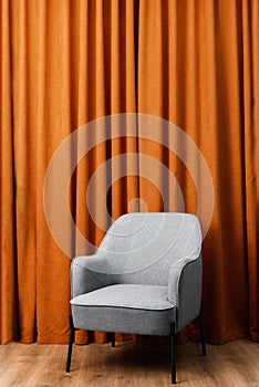 Gray easy chair stands against the background of an orange curtain