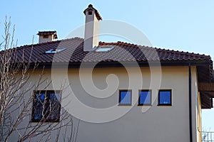 Gray facade of a house with windows and a brown tiled roof against a blue sky