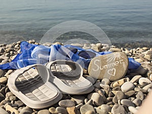 gray flip-flops and a blue pareo, sunglasses and a stone with the inscription Summer on a pebble beach