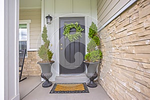 Gray front door of a home with green wreath and flanked by tall potted plants