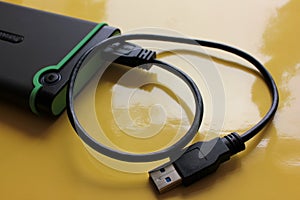 Gray and green external hard drive for backup with USB cable on yellow background with copy space.