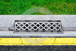 Gray gutter of a stormwater drainage system on the side of asphalt road.