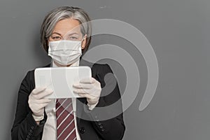 Gray-haired businesswoman works notepad. Caucasian lady holds tablet looking at camera on gray background with textspace