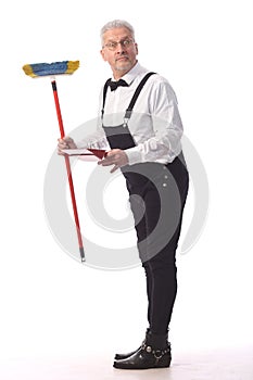 Gray-haired cleaner, janitor in a black jumpsuit with a mop and dustpan provides cleaning service, on white background