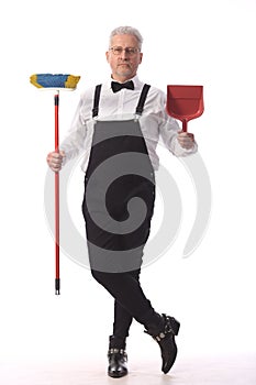 Gray-haired cleaner, janitor in a black jumpsuit with a mop and dustpan provides cleaning service, on white background