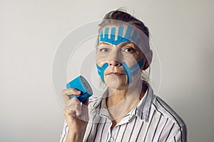 gray-haired elderly woman with kinesiotaping on her face to smooth out