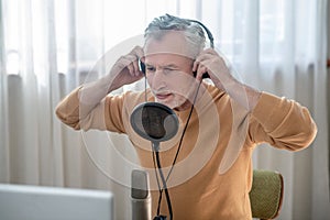 A gray-haired man in black headphones speaking in microphone