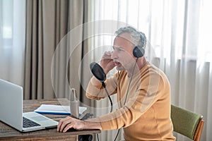 A gray-haired man in black headphones speaking in microphone