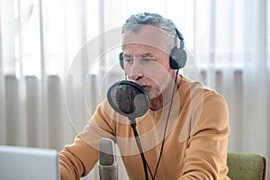 A gray-haired man in black headphones speaking in microphone and looking busy